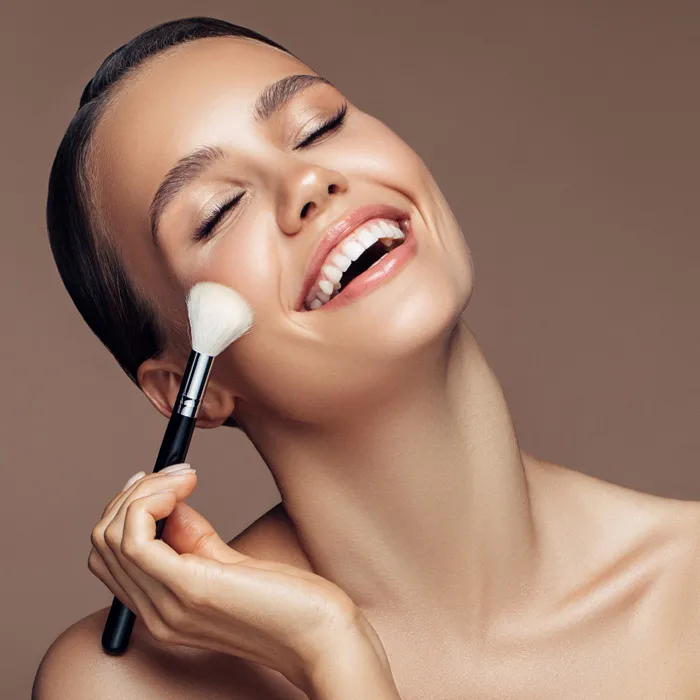 Een lachende vrouw krijgt make-up aangebracht met een penseel
