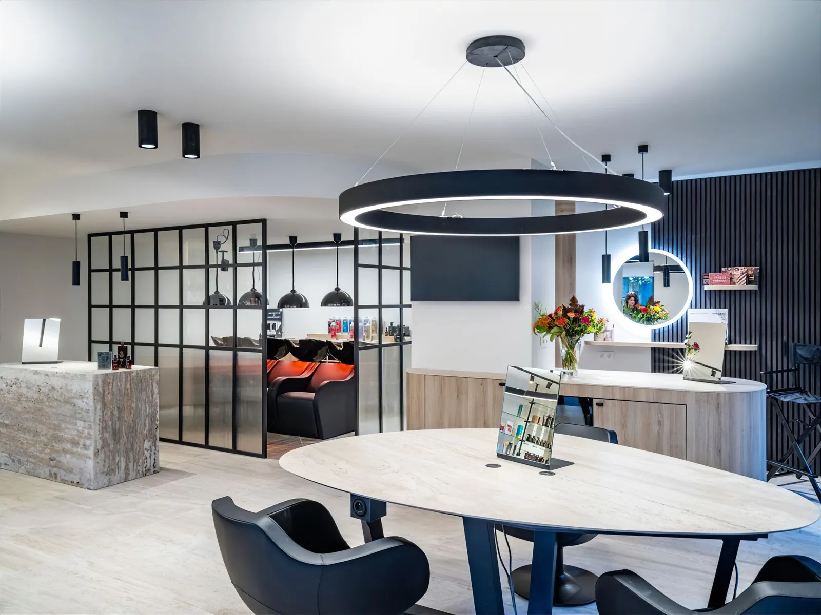 Het vernieuwde salon van Coiffure Farrell met de ovale tafel, ronde lamp en de wasruimte achter glas